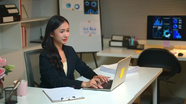 Young Businesswoman Using AI Chat Bot Laptop at Office Desk with Data Dashboard in Background