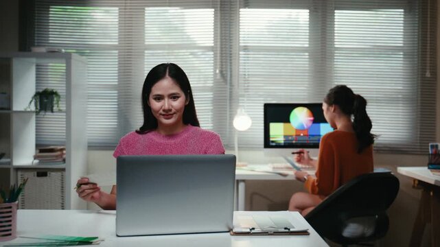 Two professional asian women working in a creative agency office. Female designers collaborating on a project using computers and color samples