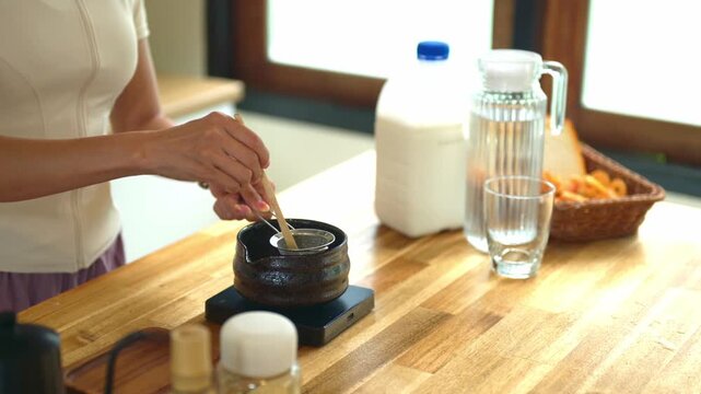 Closeup Woman uses bamboo scoop to sift vibrant green matcha powder through a fine mesh strainer into a dark ceramic