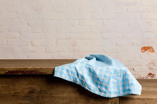 Empty wooden table with a blue gingham cloth against a weathered brick wall mockup for kitchen and product display background