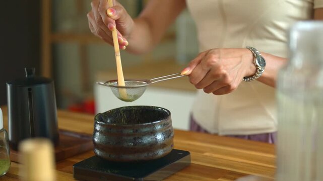 Woman Sifting Matcha Green Tea Powder into Ceramic Bowl with Bamboo Scoop and Fine Mesh Strainer