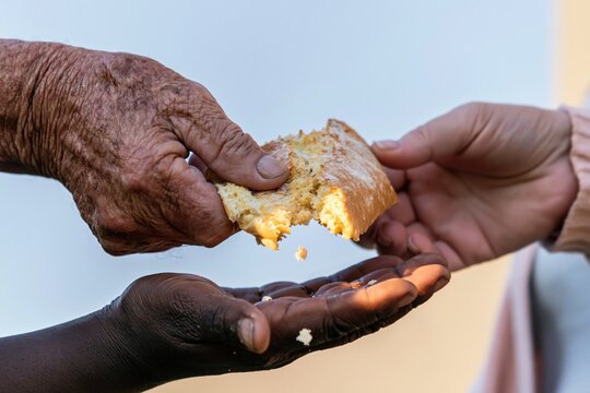 Weathered hands of an elderly man sharing a piece of crusty bread with another person for concepts of charity, hunger, and humanitarian aid