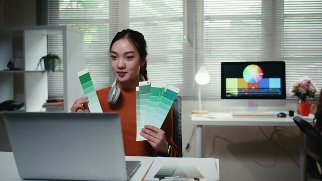Young asian female creative designer presenting green color palette samples during an online meeting on her laptop at her modern office desk