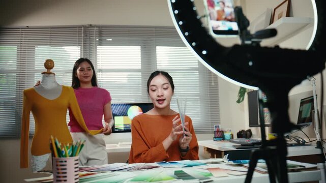 Two young Asian women, fashion designers and online sellers, presenting new clothes and color choices to their followers during a live stream