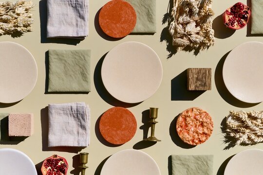 Repeated pattern of matte cream plates and linen napkins with earthy terracotta and brass accents for autumn interior styling boards