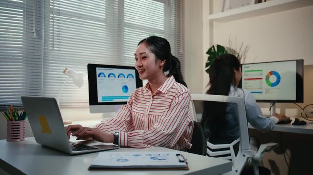 Smiling asian businesswoman working in the office using a laptop. Corporate employee managing company data, analyzing charts and typing