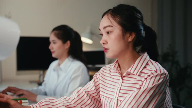 Two young businesswomen discussing a project while working late at night. Colleagues collaborating in a modern office after hours