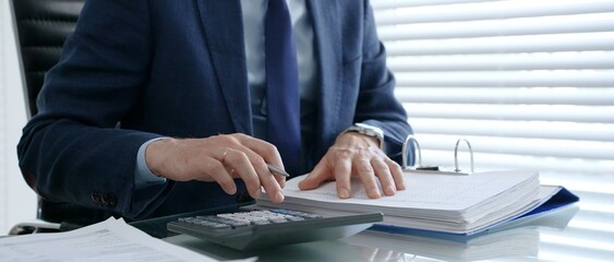 Businessman calculating expenses, verifying financial data, and filling out paperwork using a...