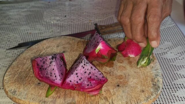 Hand of adult woman grabbing a dragon fruit twig next to sliced fruit
