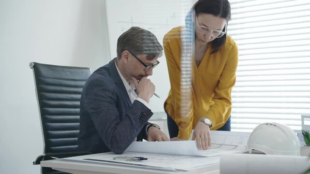 Architects and engineers reviewing blueprints and project plans at a desk, collaborating on design solutions and construction strategy in a modern professional office setting