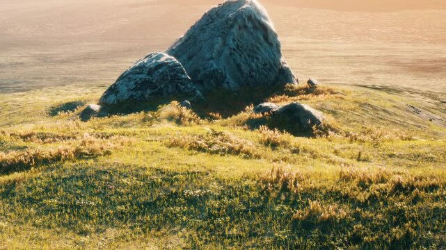 A large rock formation sits on a grassy field as the sun sets in the background. The landscape shows rolling hills and a clear sky. Soft light enhances the natural colors of the scene.