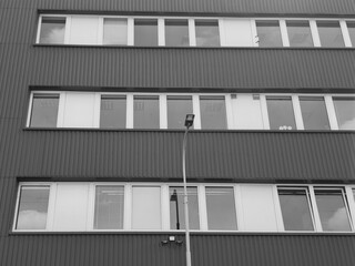 Modern office building facade with corrugated metal sheets panels and horizontal rows of glass windows in black and white © czjonyyy