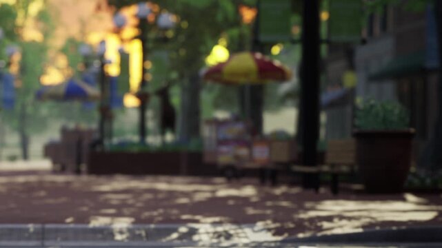 People walk along a paved path in a park on a sunny day. Benches line the walkway and colorful umbrellas provide shade. Trees surround the area, creating a lively scene.