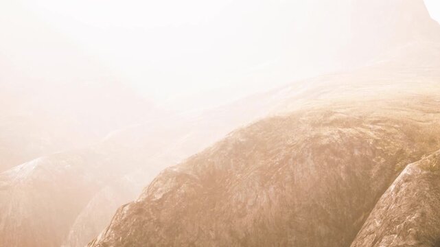 A view of mountains shrouded in fog with soft lighting. The scene captures the natural landscape. The time is early morning, adding a sense of mystery.