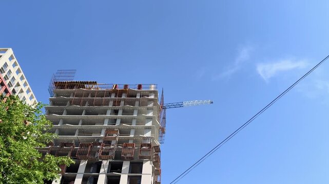 Low angle view of unfinished residential building with tower crane and scaffolding against clear blue sky