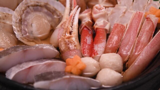 Fresh seafood hot pot ingredients beautifully arranged in dark bowl with premium sashimi-grade fish and shellfish