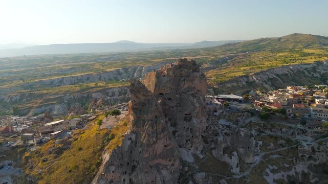 Uchisar, Nevsehir, Turkey. Uchisar Castle, a massive volcanic tuff rock formation carved with tunnels and chambers, aerial view over Cappadocia at golden hour. Aerial View, Departure of the camera