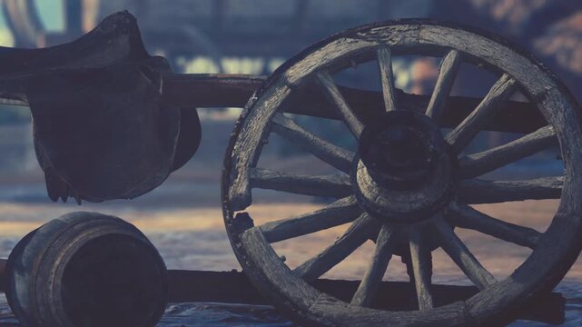 A wooden wagon wheel lies on the ground. Nearby is a rustic building. The setting appears to be an outdoor area, with soft light illuminating the scene.