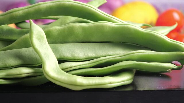Fresh green beans on a black surface with other vegetables