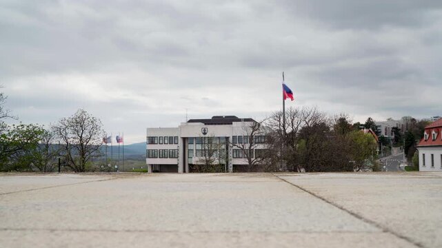 Exterior of National Council of the Slovak Republic building in Bratislava with waving Slovakian flag. National flag of Slovakia flies in front of Narodna Rada parliament on cloudy spring day. 4K