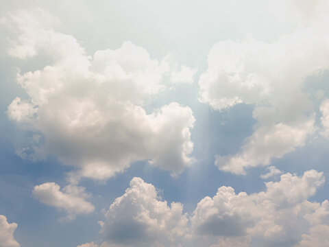 Sunbeams through cumulus clouds in blue sky creating dramatic cloudscape background