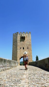 Woman traveler with backpack walking on medieval stone bridge towards historic tower in Spain, Frias, Burgos province- vertical video