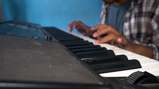 Young Man Playing Piano Keyboard Wearing Plaid Shirt Against Plain Blue Background