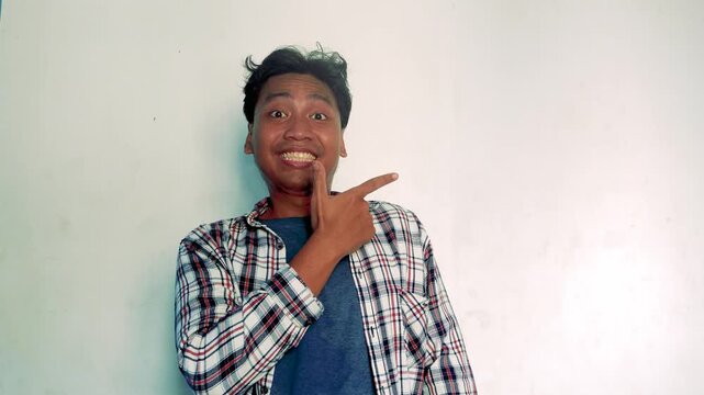 Young Asian Man Pointing Sideways With A Cheerful Smile Wearing A Plaid Shirt On White Background