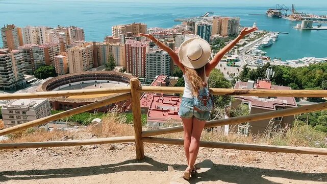 Back view of woman traveler with raised arms enjoying panoramic view of Malaga city and bullring in Spain