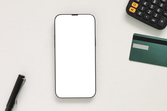 Blank smartphone screen mockup on a white desk with a pen, black calculator, and credit card. Top view flat lay template perfect for digital banking, finance, or ecommerce app design.
