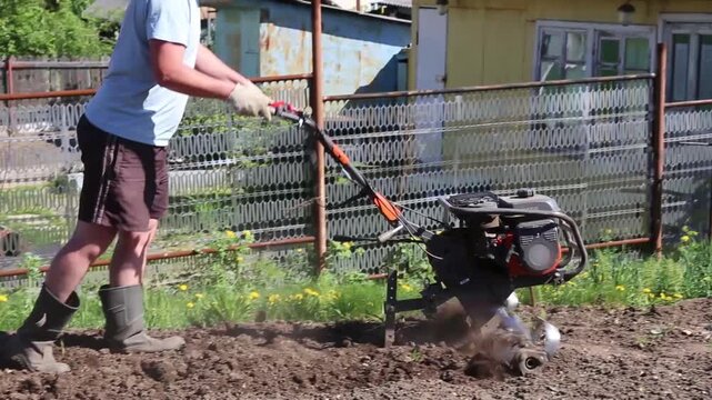 Gardener using motorized cultivator on the plantation. Plowing garden with a motor cultivator before planting potatoes and other crops