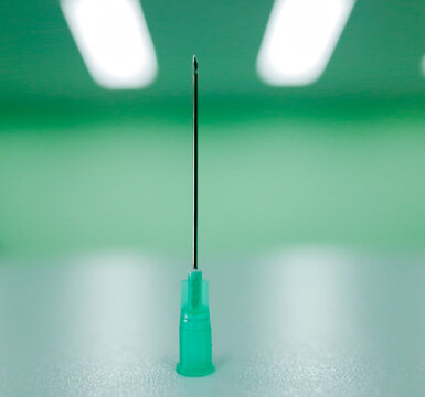 Sterile medical hypodermic syringe needle standing vertically on green backgr