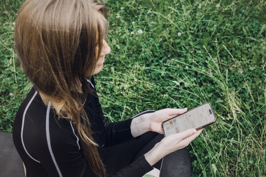 Woman hold smartphone showing calendar interface of cycle tracker application over green grass in park. Femtech calendar interface, menstrual cycle log, ovulation tracking software, 