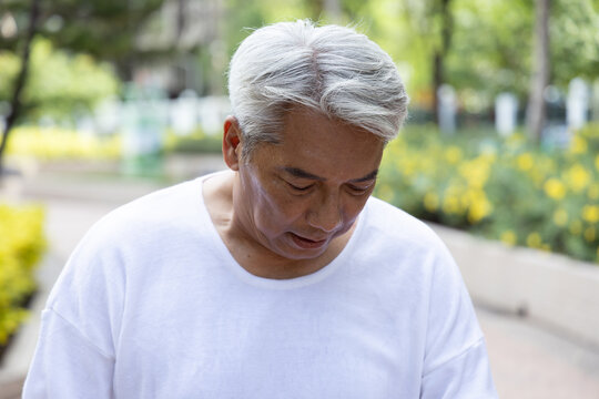 Old asian senior man looking tired, sweating from summer heat outdoors, portrait of perspiration and discomfort in green park