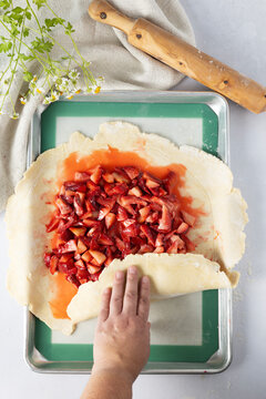 Hand folding dough over a strawberry galette filling