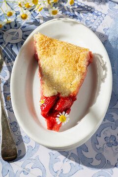Slice of strawberry pie on a plate with chamomile flowers
