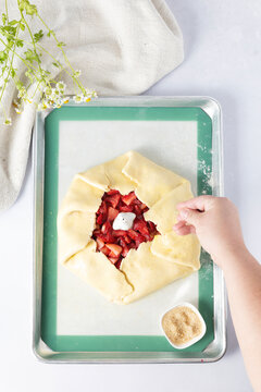 Hand sprinkling sugar on a rustic strawberry galette