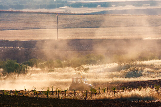 Tractor plowing a field raising dust at golden hour in Alhambra, Spain