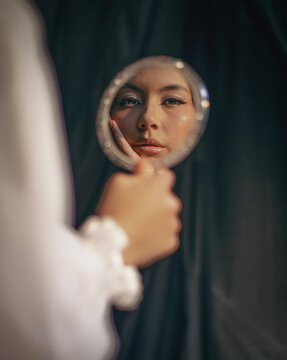 Young woman looking at her reflection in a hand mirror