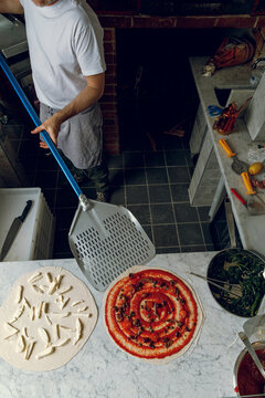 A pizzaiolo places a pizza base onto a peel. Artisan pizzeria