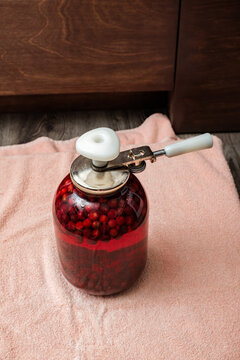 A Can Seamer. Canning cherry compote using a manual seaming machine to seal a large glass jar with metal lid. Home food preservation, traditional kitchen, winter storage preparations.