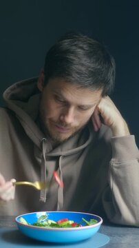 Unhappy sad man reluctantly eating vegetable salad, following strict medical diet for health conditions like cholecystitis, pancreatitis. Food restrictions. Man eating salad on medical diet for health