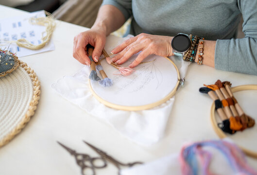 Woman Chooses Embroidery Threads While Holding an Embroidery Hoop with Fabric with a Sketched Pattern and Scissors Nearby