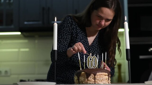 Young woman lighting candles on a birthday cake with number 60 candles. Close family celebration preparation before a milestone birthday gathering.