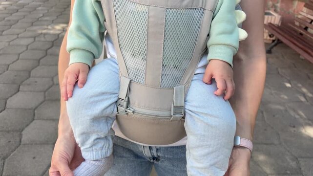 Mother and child. A mother carrying her baby in a beige, mesh-front ergonomic baby carrier with a hip seat.