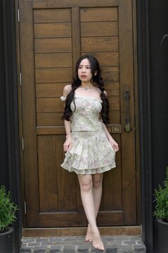 Young woman in floral dress standing barefoot by wooden door with plants