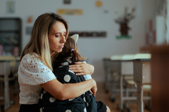 Sad Teacher Hugging Elementary Student In Front of the Classroom. Unhappy mother embraces little schoolgirl student inside empty primary education learning room