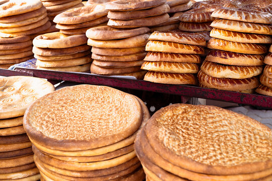 Traditional Uzbek flatbread stacked in abundant piles at a bazaar in Bukhara. Golden-brown non bread with decorative patterns displayed for sale, ideal for food culture and travel content.