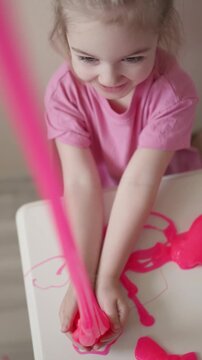 Toddler explores pink slime in a playful indoor setting on a sunny afternoon