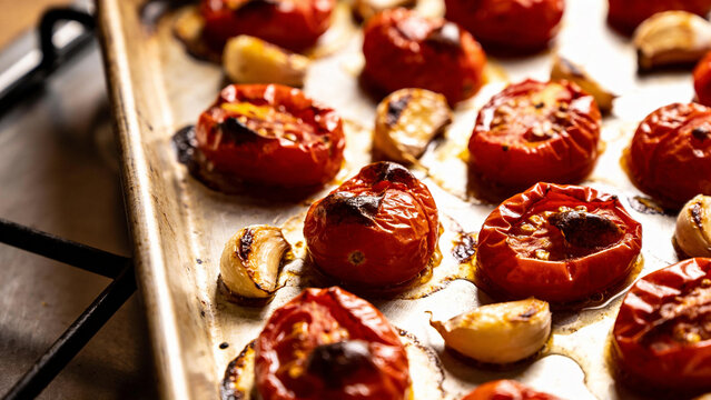 Roasting tomatoes and garlic on a baking tray in a kitchen setting during the evening hours